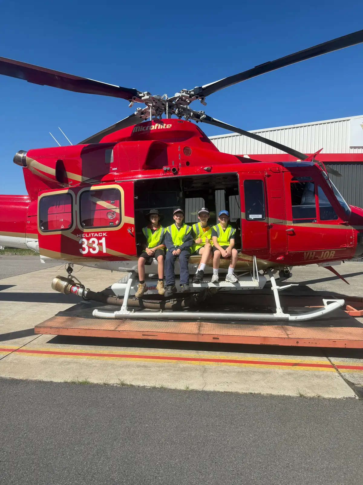 Four juniors sitting in the open doorway of the red Helitack 331 helicopter